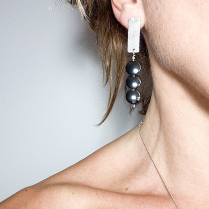 woman waering Handmade sterling silver hematite drop earrings with minimalist sculptural design.